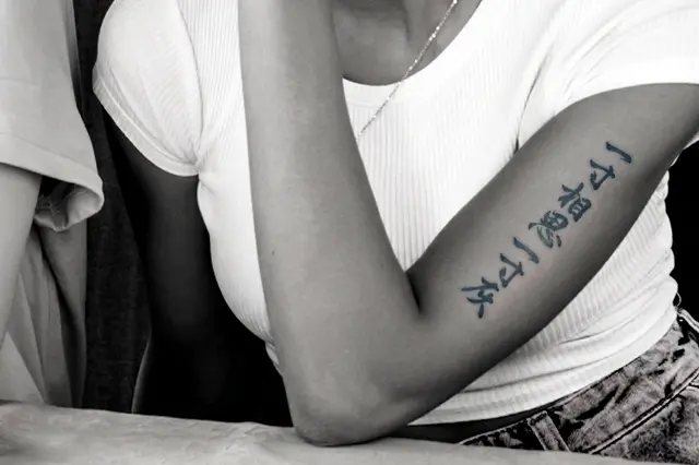 Elegant vertical Hanzi tattoo on a woman’s forearm, captured in black and white with a minimalist aesthetic.
