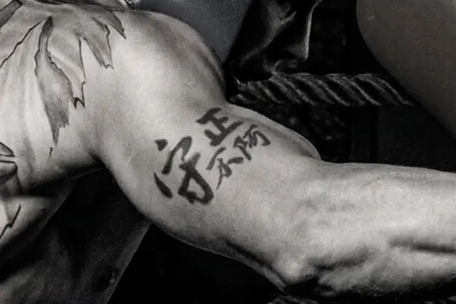 Black ink Chinese calligraphy tattoo on a man's upper arm in a semi-cursive script, meaning "Upholding Integrity."