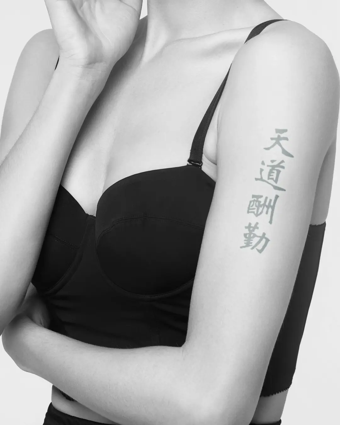A mockup of a Tian Dao Chou Qin tattoo on a woman's left upper arm.