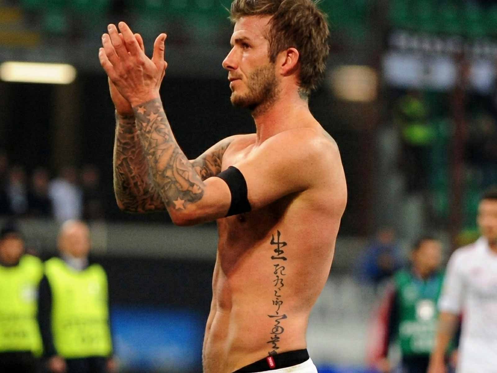David Beckham on a soccer pitch showing his Chinese calligraphy tattoo reading 生死有命 富貴由天 on his left torso